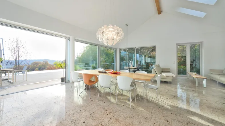 Heller, offener Wohn-Essbereich mit hohen Decken, Marmorboden und Zugang zur Terrasse mit Weitblick.