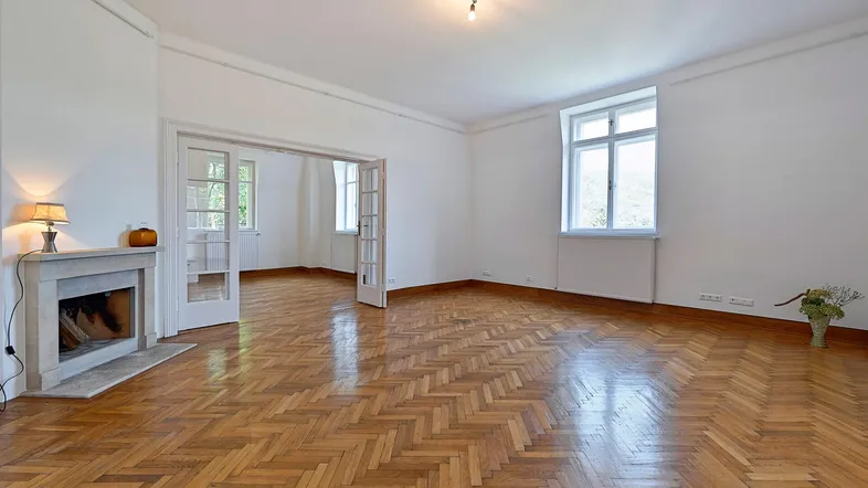 Helles Wohnzimmer mit Fischgrätparkettboden, Kamin und Zugang zu weiteren Räumen.