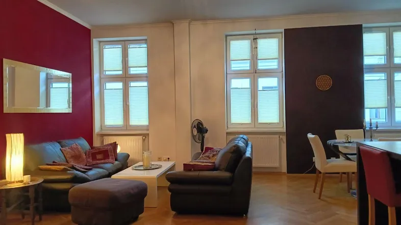 Geräumiger Wohn- und Essbereich mit roter Akzentwand, dunklen Sofas und Fischgrätparkettboden.