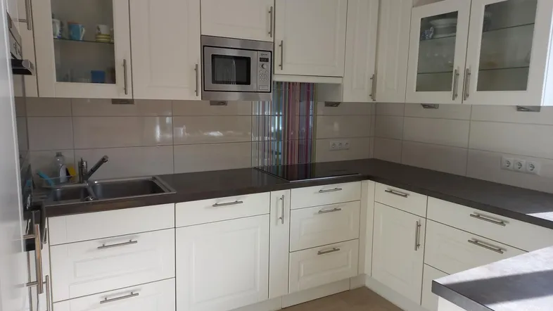 Helle Küche mit weißen Schränken, dunkler Arbeitsplatte und integrierten Geräten.