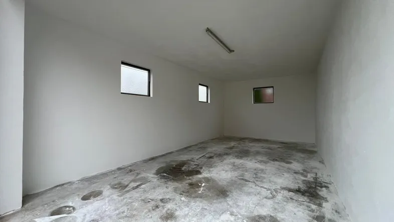 Leerer Garagenraum mit Betonboden und kleinen Fenstern, bereit zur Nutzung und Lagerung.
