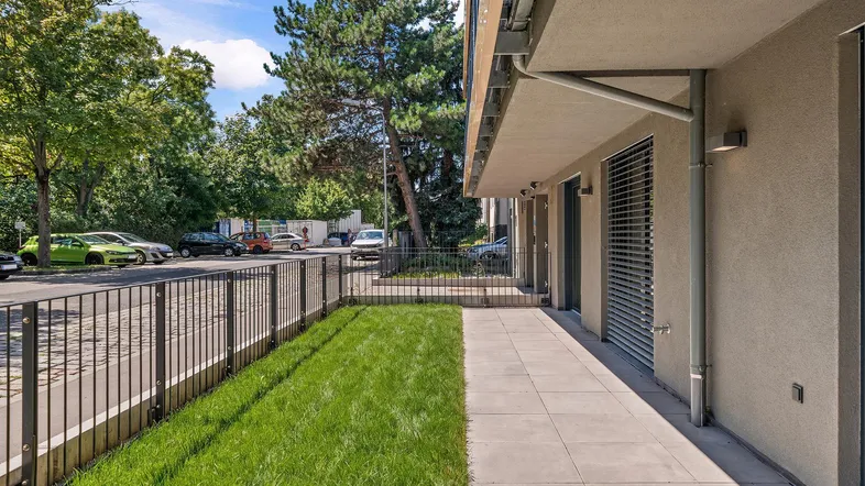 Kleiner privater Gartenbereich mit Rasenfläche und gepflastertem Weg vor dem Gebäude.