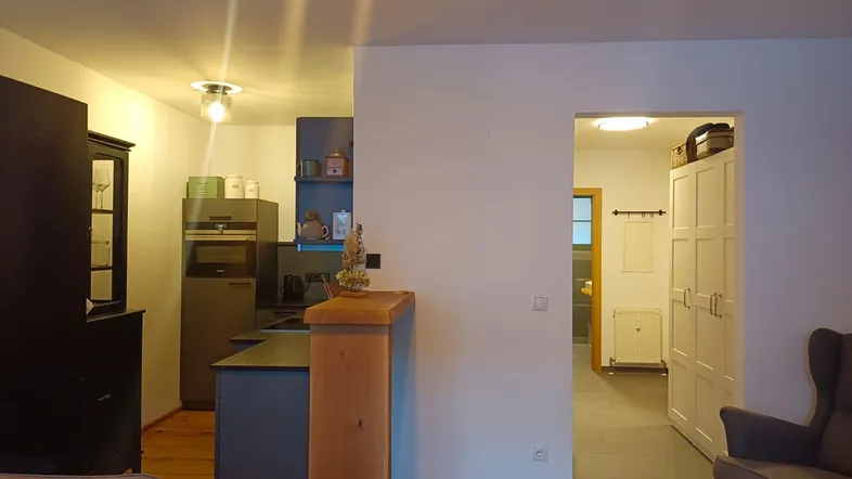 Offener Wohnbereich mit Holzboden und Blick in eine moderne Küche mit dunklen Schränken.