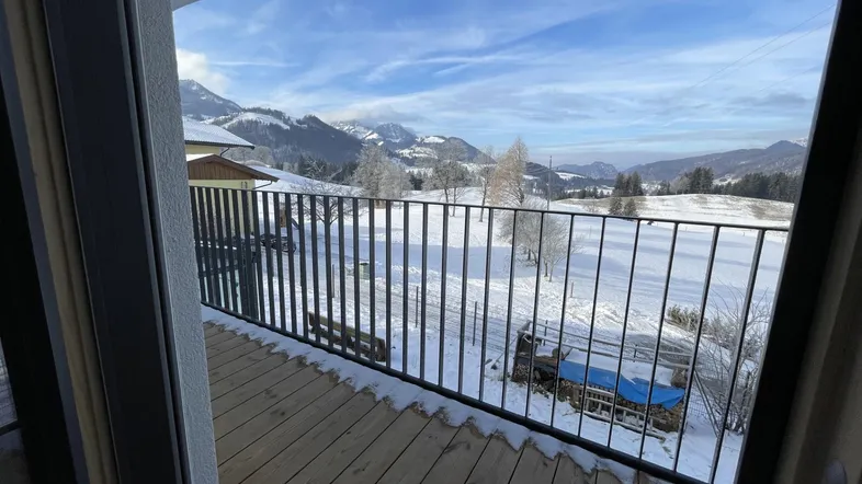 Blick vom Balkon auf eine verschneite Berglandschaft mit weitem Horizont und klarem Himmel.