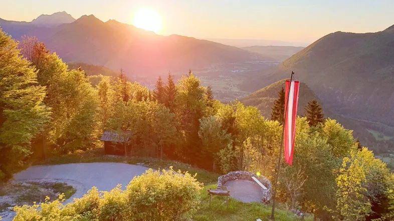 Sonnenuntergang über den Bergen mit weitem Blick ins Tal und österreichischer Flagge.