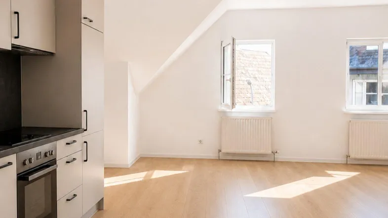 Helle Küchenzeile in einem offenen Raum mit Dachschräge und Laminatboden, gut beleuchtet durch Fenster.