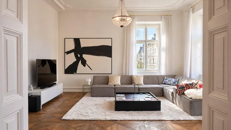 Helles Wohnzimmer mit Fischgrätparkett, modernem Sofa und Kronleuchter, bietet eine elegante Atmosphäre.