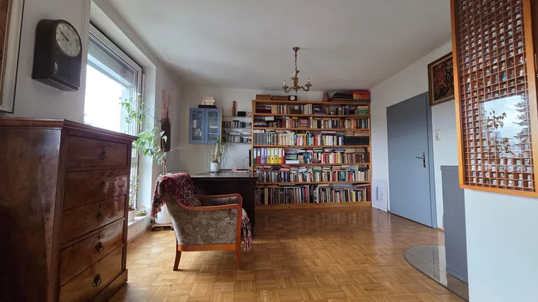 Geräumiges Arbeitszimmer mit großem Bücherregal, Parkettboden und viel Tageslicht durch große Fenster.