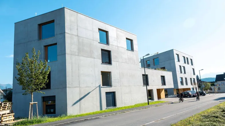 Moderne Wohngebäude mit Sichtbetonfassaden und großen Fenstern in sonniger Umgebung.