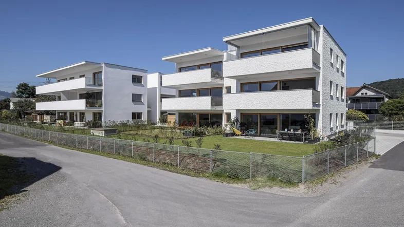 Mehrere moderne Wohngebäude mit Balkonen, Gärten und grünen Rasenflächen unter strahlendem Himmel.