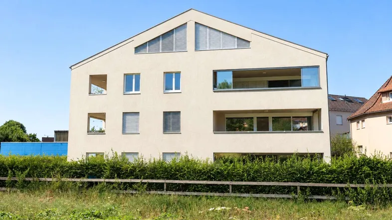 Moderne Wohnanlage mit heller Fassade, großen Fenstern und Balkonen in grüner Umgebung.