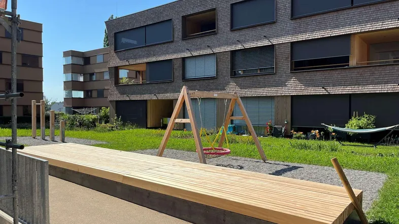 Moderner Wohnkomplex mit Holzfassade, Grünflächen und einem Spielplatz für Kinder.