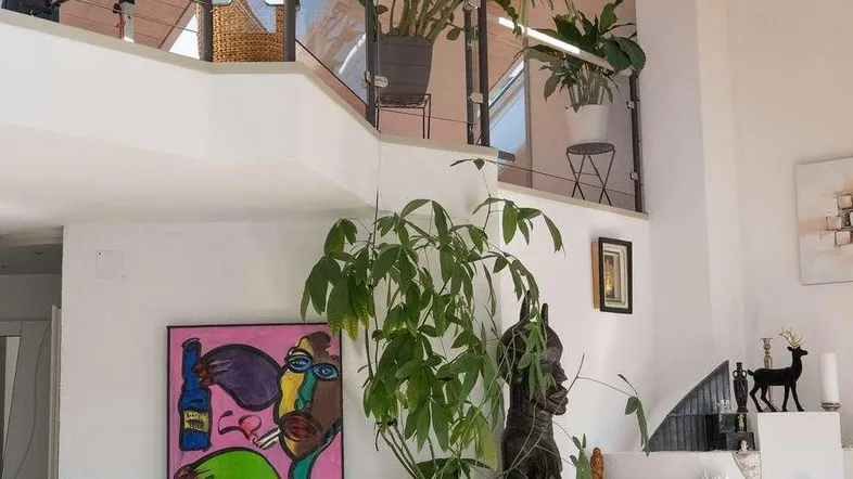 Helles Wohnzimmer mit Galerie, hohen Decken und dekorativen Pflanzen.