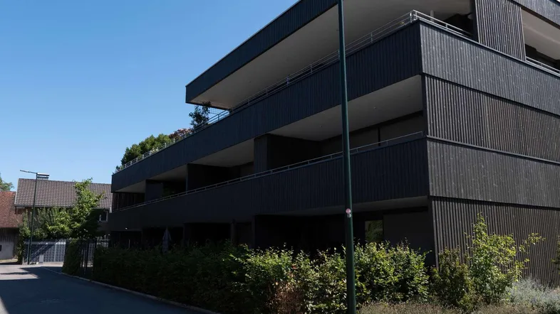 Moderne Wohnanlage mit dunkler Holzfassade und Balkonen unter blauem Himmel.