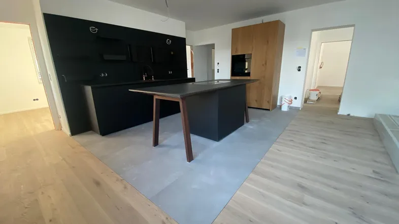 Moderne, offene Küche mit schwarzen Fronten, Holzelementen und einer Kochinsel in einem Neubau.