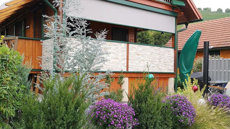 Charmantes Holzhaus mit Balkon, gepflegtem Vorgarten und dekorativen Pflanzen.
