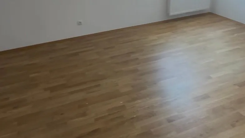 Heller Raum im Dachgeschoss mit schrägen Wänden, Parkettboden und Fenster.