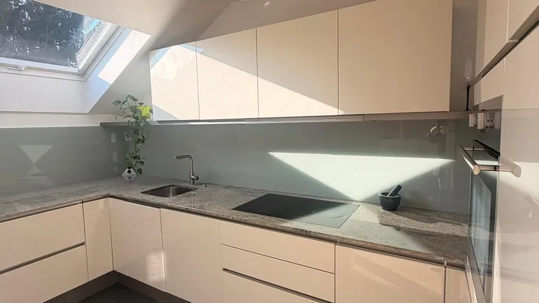 Moderne Küche mit hellen Schränken, Granitarbeitsplatte und Dachfenster, durchflutet von Sonnenlicht.