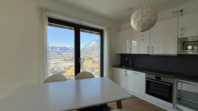 Moderne Küche mit Essbereich, weißen Hochglanzfronten und beeindruckendem Bergblick.