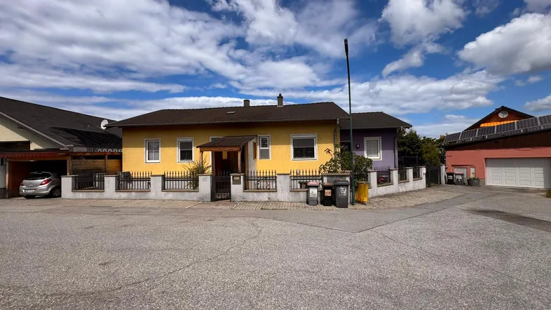 Gelbes und lila gestrichenes Einfamilienhaus mit Vorgarten und Zaun unter blauem Himmel.
