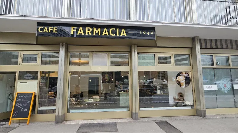 Fassade eines Geschäftsgebäudes mit großen Schaufenstern und dem Schriftzug 'CAFE FARMACIA'.
