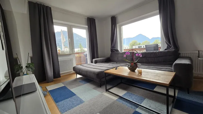 Helles Wohnzimmer mit gemütlichem Sofa, Holztisch und weitem Bergblick durch große Fenster.
