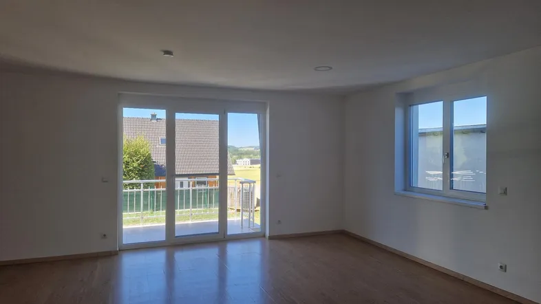 Helles Wohnzimmer mit Holzboden, Zugang zum Balkon und weitem Blick ins Grüne.