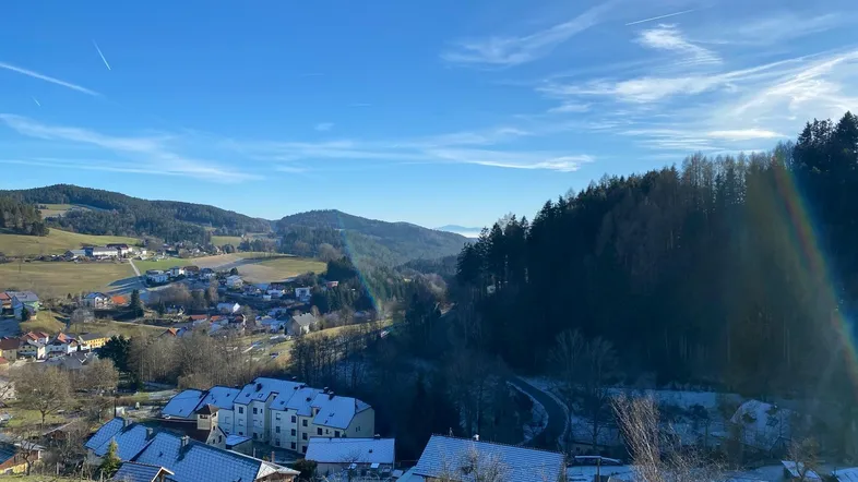 Malerischer Blick auf ein Dorf in einer hügeligen Landschaft mit Wäldern und klarem blauen Himmel.