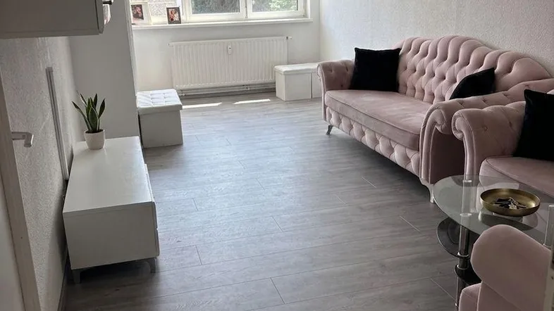 Helles Wohnzimmer mit modernem Laminatboden, rosa Sofa und dekorativer Wanduhr.