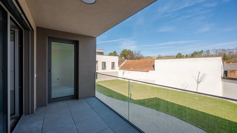 Moderner Balkon mit Glasgeländer, Fliesenboden und weitem Blick ins Grüne.