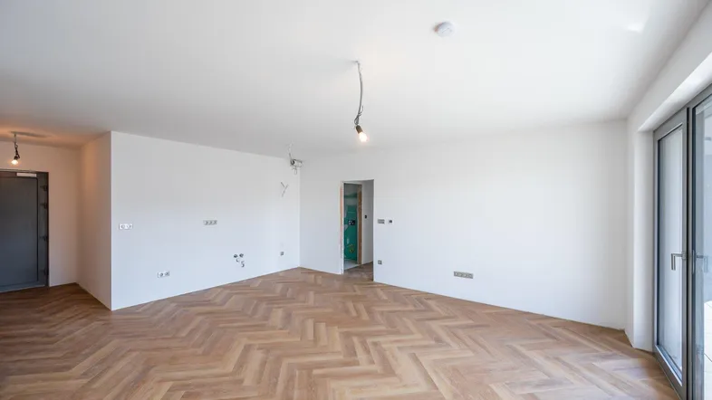 Helles, unmöbliertes Zimmer mit Fischgrätparkett und Zugang zu einem Balkon oder einer Terrasse.