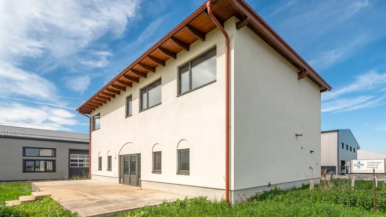 Modernes Gebäude mit weißer Fassade, braunem Dachüberstand und einer großen Terrasse im Freien.