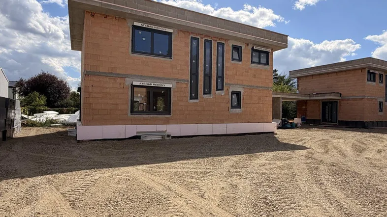 Rohbau eines modernen Hauses mit Flachdach und großen Fenstern, umgeben von Baustellengelände.