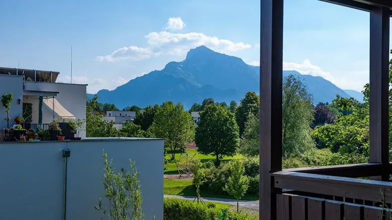 Blick von einem Balkon auf eine beeindruckende Berglandschaft und grüne Umgebung unter blauem Himmel.