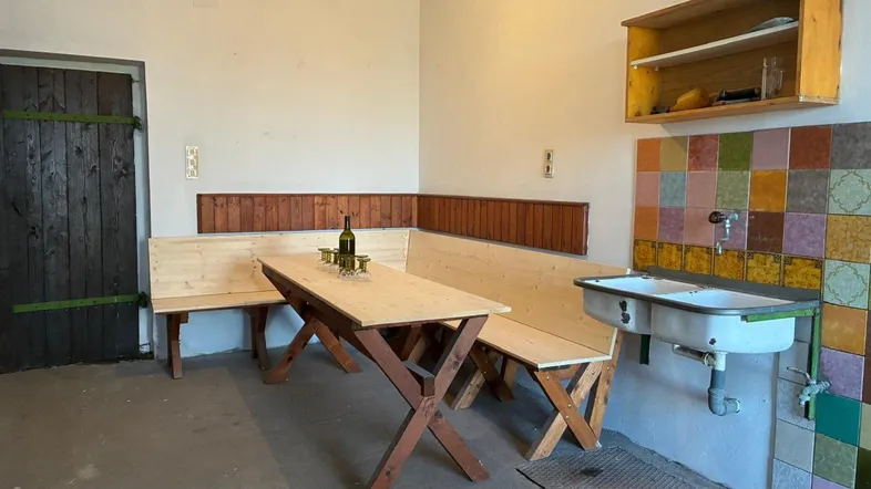 Rustikaler Raum mit Holzbänken, Tisch und einfacher Spüle, ideal für gesellige Runden.