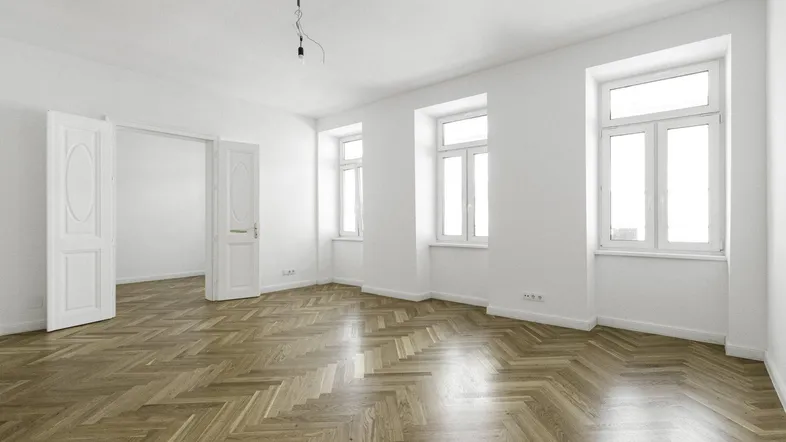 Heller Raum mit Fischgrätparkett, weißen Wänden und hohen Fenstern, der viel Tageslicht bietet.