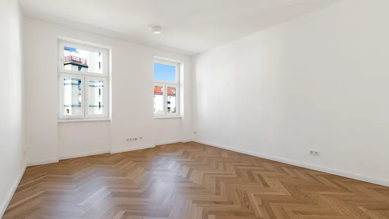 Helles, leeres Zimmer mit Fischgrätparkett und weißen Wänden, bereit zur individuellen Gestaltung.