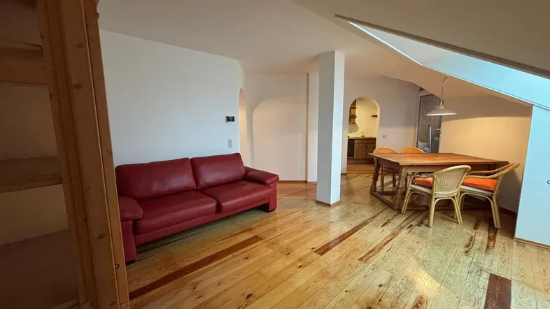 Geräumiger Wohn-Essbereich mit rotem Sofa, Holzboden und Dachschrägen, ideal für gemütliche Abende.