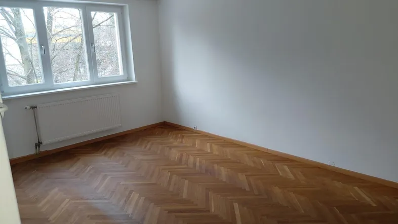 Heller Raum mit Fischgrätparkettboden und großem Fenster, ideal als Wohn- oder Schlafzimmer.