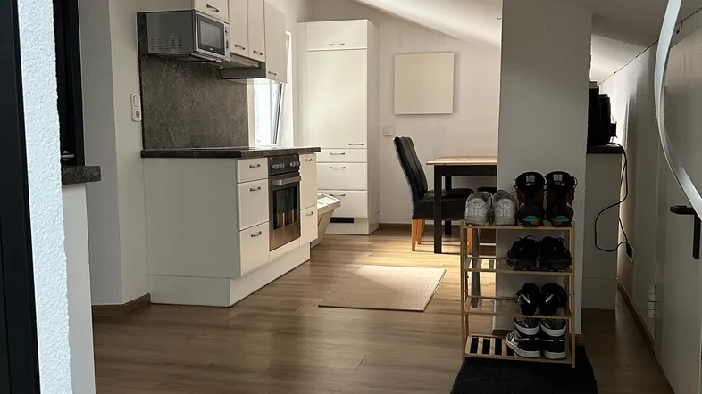 Helle offene Küche mit weißen Schränken, Laminatboden und Essbereich unter Dachschräge.