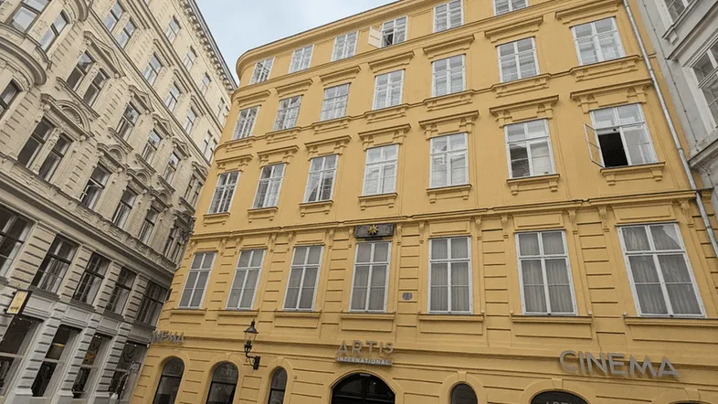 Gelbes historisches Gebäude mit vielen Fenstern an einer gepflasterten Straße in der Stadt.