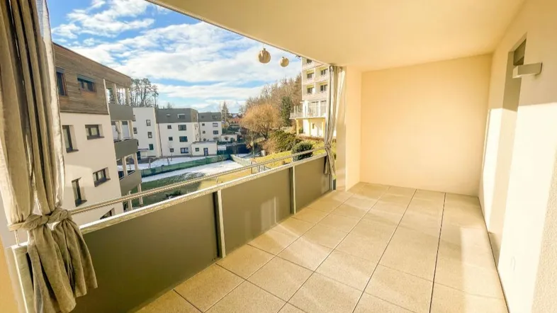 Geräumiger Balkon mit Fliesenboden und weitem Blick auf die umliegenden Gebäude und Berge.