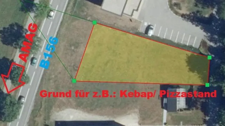 Luftaufnahme eines Grundstücks an einer Straße, markiert für potenzielle gewerbliche Nutzung, umgeben von Grünflächen.