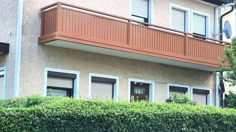 Fassade eines Wohnhauses mit einem Balkon und einer gepflegten Hecke im Vordergrund.