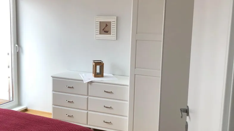 Helles Schlafzimmer mit Holzboden, weißem Kleiderschrank und Zugang zum Balkon.