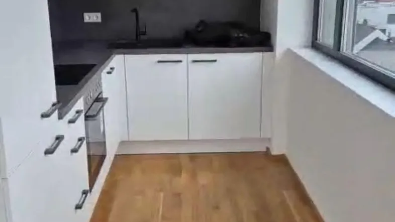 Moderne Einbauküche mit weißen Schränken, dunkler Arbeitsplatte und Holzboden, mit Fensterblick.