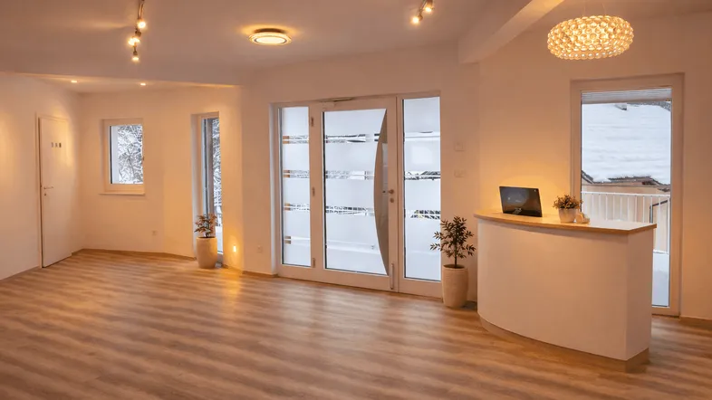 Heller, offener Empfangsbereich mit modernem Tresen, großen Fenstern und Blick auf verschneite Umgebung.