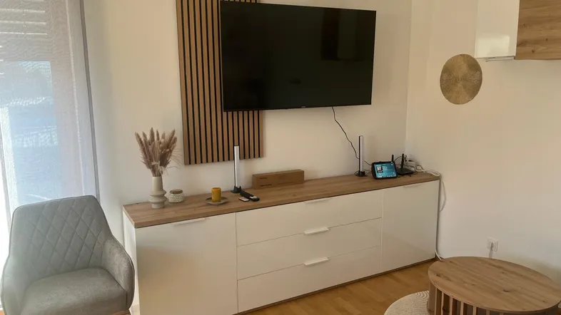 Modernes Wohnzimmer mit TV-Möbel, Holzpaneel und hellem Parkettboden, gut beleuchtet.