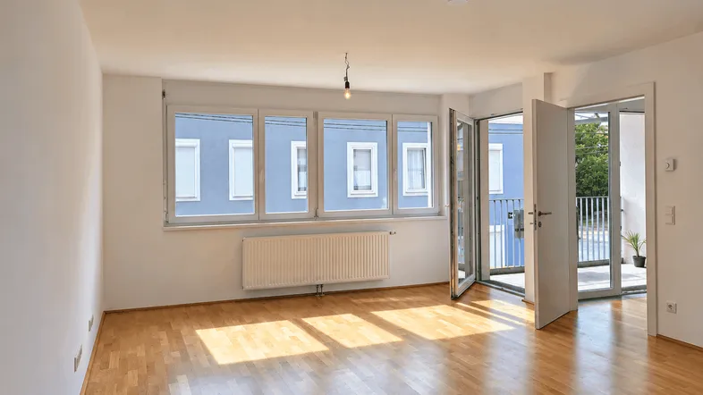 Helles Wohnzimmer mit Parkettboden, großen Fenstern und Zugang zu einem Balkon.