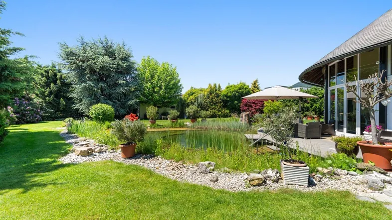 Großer Garten mit Teich, Sitzbereich und Blick auf die moderne Architektur des Hauses.